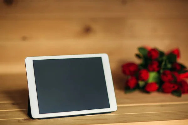 Beautiful red tulips and tablet on a wooden background