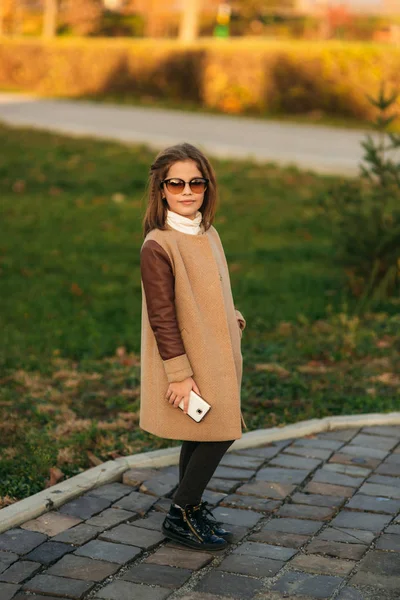 Niña con abrigo de otoño usando teléfono. Otoño dorado —  Fotos de Stock