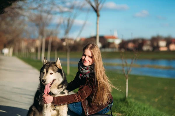 Une fille souriante marche avec un chien le long du remblai. Magnifique chien husky — Photo