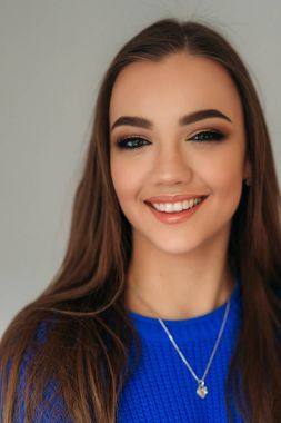 Güzel esmer kız mavi bir bluz bir fotoğrafçısına poz ve ona makyaj gösteren güzel bir gülümseme