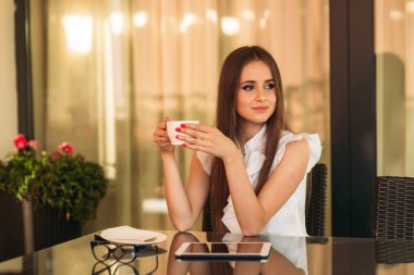 Genç kız bir tablet ve içki kapuçino kullanın. Kafede kız gülümsüyor