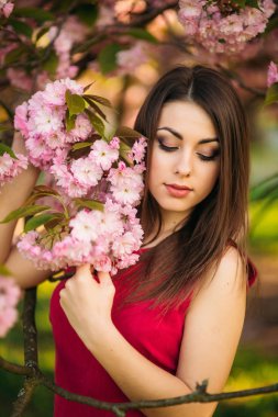 Genç kız bir fotoğraf için poz portresi. Pembe çiçekli ağaçlar içinde belgili tanımlık geçmiş. Bahar. Sakura