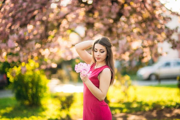 Piękna dziewczyna pozuje do drzew fotograf na tle kwitnących róż. Wiosną. Sakura — Zdjęcie stockowe