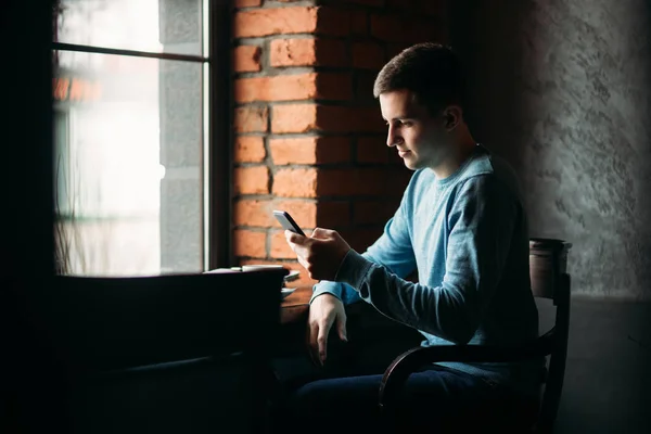 Man med telefonen på ett café sitter mittemot fönstret — Stockfoto