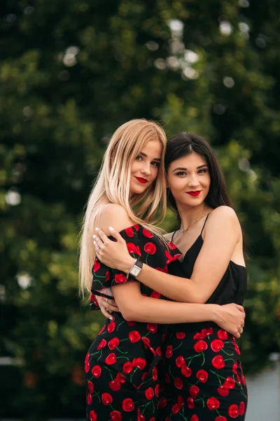 Schöne Mädchen, die für den Fotografen posieren. zwei Schwestern in schwarz-rotem Kleid. Lächeln, sonniger Tag, Sommer — Stockfoto