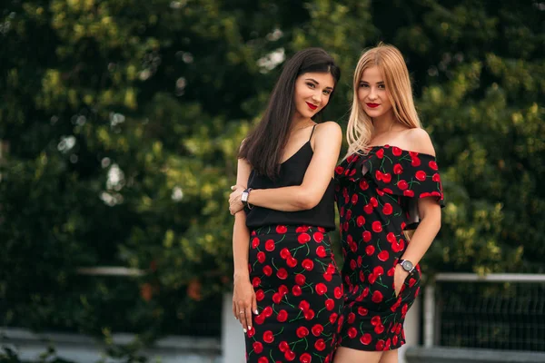 Vackra flickor poserar för fotografen. Två systrar i svart och röd klänning. Leende, solig dag, sommar — Stockfoto