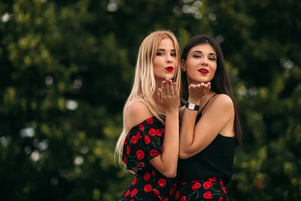 Mooie meisjes poseren voor de fotograaf. Twee zussen in zwarte en rode jurk. Glimlach, zonnige dag, zomer — Stockfoto