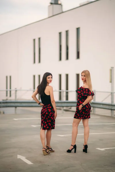 Vackra flickor poserar för fotografen. Två systrar i svart och röd klänning. Leende, solig dag, sommar — Stockfoto