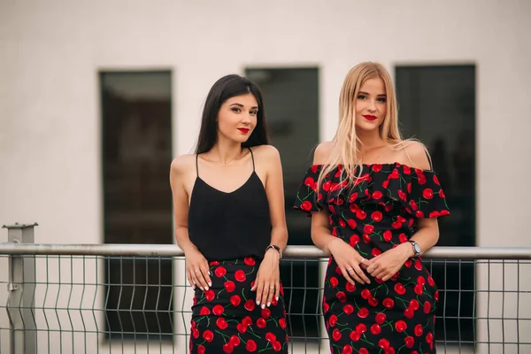 Mooie meisjes poseren voor de fotograaf. Twee zussen in zwarte en rode jurk. Glimlach, zonnige dag, zomer — Stockfoto