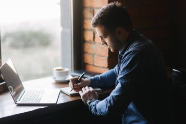 Bir sakallı bir dizüstü bilgisayar bir kafede kullanır.