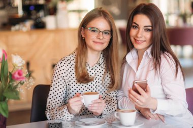 kapuçino içiyor ve telefon kullanarak bir kafede oturan kızlar