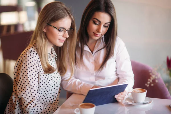 Две девушки используют планшет, сидя в кафе и пья кофе — стоковое фото