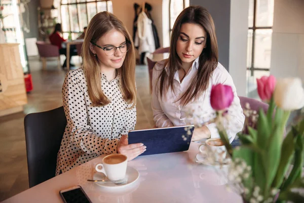 Zwei Mädchen benutzen ein Tablet, während sie in einem Café sitzen und Kaffee trinken — Stockfoto