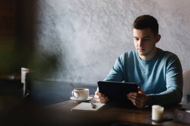 Adam bir kafede oturuyor ve bir tablet kullanır