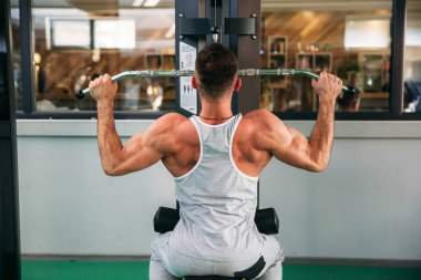 Genç bir atlet spor salonunda eğitiyor. Sırt ve göğüs kaslarının gösterir