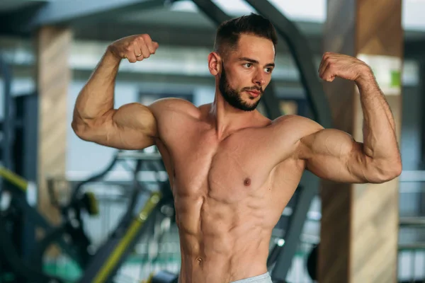 Un joven atleta entrena en el gimnasio. Muestra los músculos — Foto de Stock