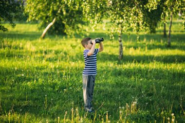 Çizgili bir gömlek küçük çocuk dürbün ile görünüyor. Bahar, güneşli havalarda