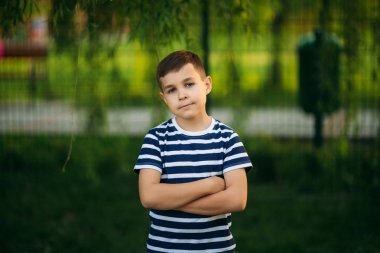 Çizgili bir T-shirt daimi yeşil arka plan önünde küçük bir çocuk. Gülümseyen ve fotoğrafçı için arıyorsunuz.