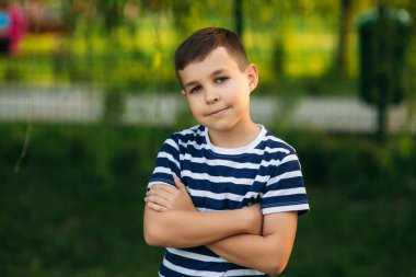 Çizgili bir T-shirt daimi yeşil arka plan önünde küçük bir çocuk. Gülümseyen ve fotoğrafçı için arıyorsunuz.