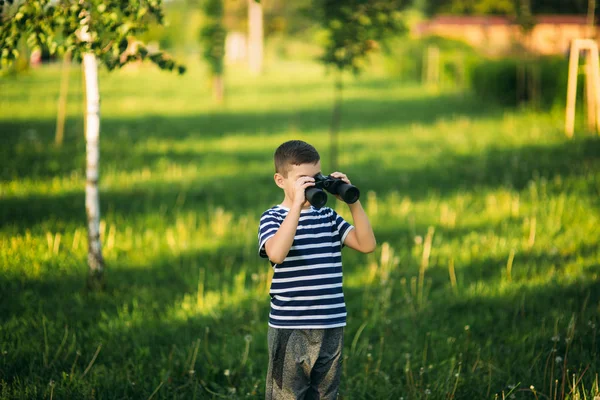 Niño con una camiseta a rayas mira a través de los prismáticos. —  Fotos de Stock