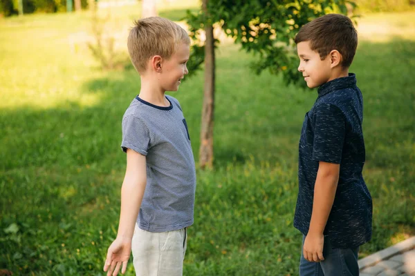 Dos niños juegan en el parque. Dos hermosos chicos en camisetas y pantalones cortos se divierten sonriendo. Comen helado, saltan, corren. El verano es soleado —  Fotos de Stock