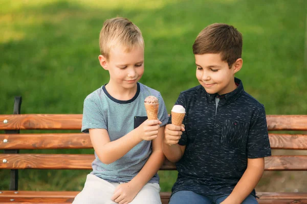 Két gyermek játszik a parkban. Két gyönyörű fiú póló és rövidnadrág szórakozást, mosolyogva. Ők eszik fagylaltot, ugrás, fuss. Nyár sunny — Stock Fotó
