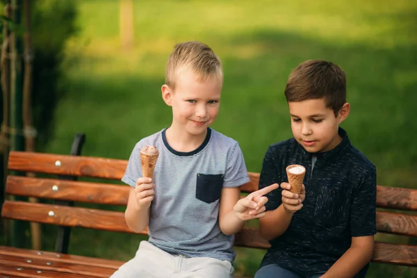 Két gyermek játszik a parkban. Két gyönyörű fiú póló és rövidnadrág szórakozást, mosolyogva. Ők eszik fagylaltot, ugrás, fuss. Nyár sunny — Stock Fotó