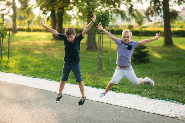 Two children are playing in the park. Two beautiful boys in T-shirts and shorts have fun smiling. They eat ice cream, jump, run. Summer is sunny