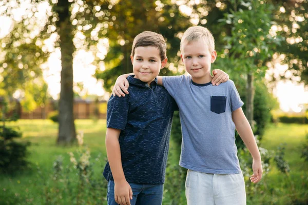 Due bambini stanno giocando nel parco. Due bellissimi ragazzi in maglietta e pantaloncini si divertono a sorridere. Mangiano gelato, saltano, scappano. L'estate è soleggiata — Foto Stock