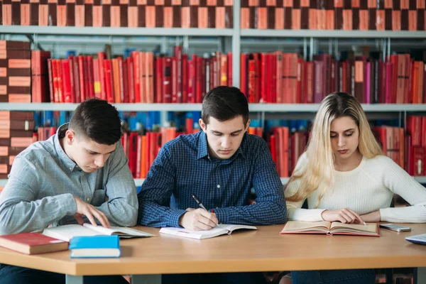 Üniversite öğrencileri kitap ve dizüstü bilgisayar ile birlikte masada oturuyor. Mutlu genç insanlar Kitaplığı'nda grup çalışması yapıyor — Stok fotoğraf