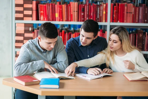 Estudiantes universitarios sentados juntos en la mesa con libros y laptop. Jóvenes felices haciendo estudios en grupo en la biblioteca — Foto de Stock