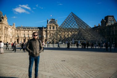 Genç bir adam haki ceket Louvre arka plan üzerinde duruyor. Güneşli sonbahar hava
