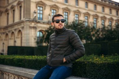 Yakışıklı adam haki bir ceket ve güneş gözlüğü bard üzerinde oturuyor