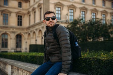 Yakışıklı adam haki bir ceket ve güneş gözlüğü bard üzerinde oturuyor