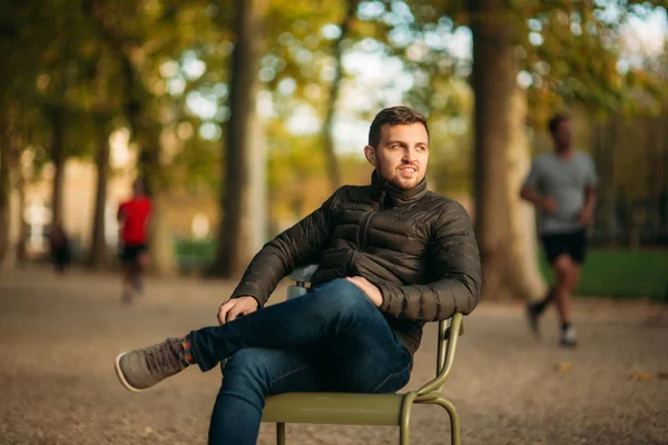 Un bel homme est assis au milieu du parc dans des tabourets kaki — Photo