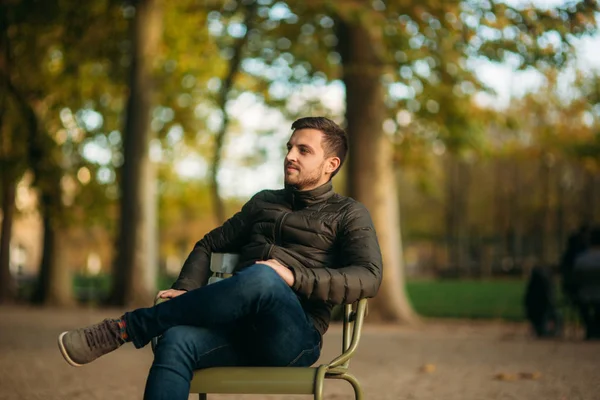Szép ember ül a parkban, a khaki színű széklet — Stock Fotó