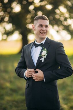 Damat bir düğme ceketini yapar. alan büyük ağaç arka planda ortasında duran