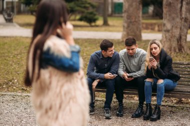 Gençler parkta iyi vakit geçiriyor. Erkek ve dişi bankta oturan ve telefonları kullanarak