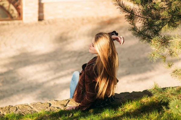 Una hermosa chica está caminando por el terraplén. Cabello rubio y chaqueta marrón. Primavera —  Fotos de Stock
