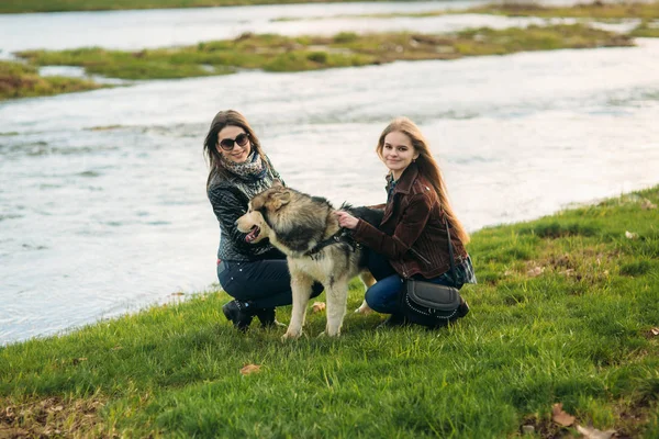 Dos hermanas pasean con perro husky frente al río — Foto de Stock