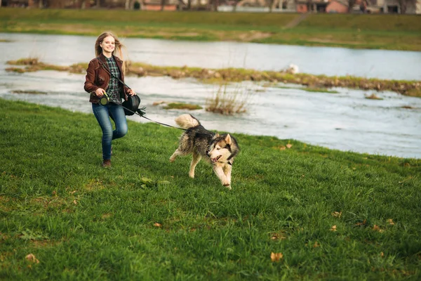 Ein Mädchen geht mit einem Hund die Böschung entlang. schöner Husky-Hund. der Fluss. Frühling — Stockfoto