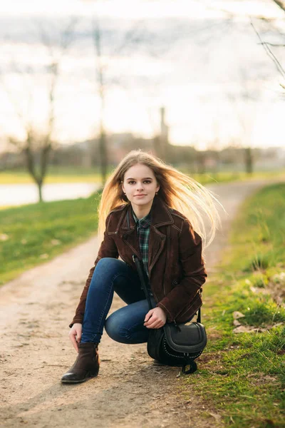 Una bella ragazza sta camminando lungo l'argine. Capelli biondi e giacca marrone. Primavera — Foto Stock