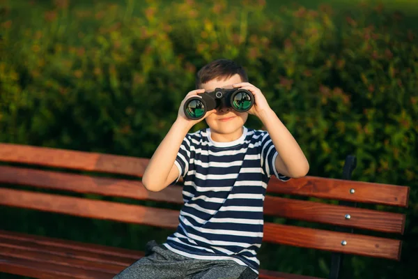 Niño con una camiseta a rayas mira a través de los prismáticos. — Foto de Stock