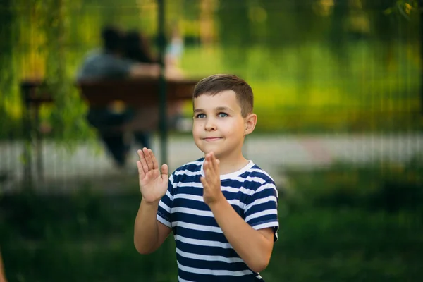 Ein kleiner Junge im gestreiften T-Shirt steht vor grünem Hintergrund. lächelnd zum Fotografen blickend — Stockfoto