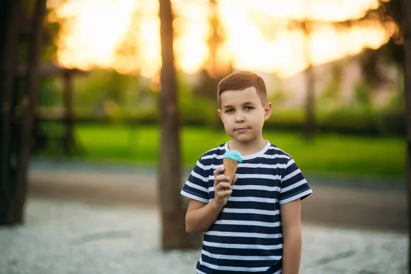 Um menino em uma camiseta listrada está comendo sorvete azul.Primavera, tempo ensolarado — Fotografia de Stock