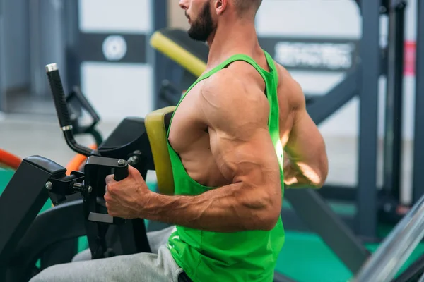 Um jovem atleta treina no ginásio. Fisiculturista treina os músculos das costas — Fotografia de Stock