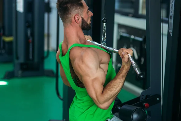 En ung idrottare tränar i gymmet. Bodybuilder tränar muskulaturen i ryggen — Stockfoto