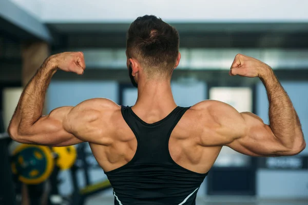 Un joven atleta entrena en el gimnasio. Muestra los músculos de la espalda —  Fotos de Stock