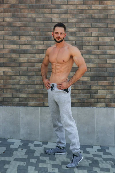 Jeune athlète posant avec un torse pour la photographie sur un fond de mur de briques. Bodybuilder, athlète avec muscles pompés, sauvetage des seins et des bras — Photo