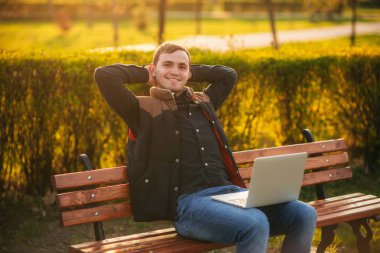 Dizüstü bilgisayar ile bankta oturan genç adam